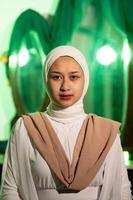 en muslim kvinna med en vit slöja och vit kläder är Sammanträde i de mitten av en grön rum utan smink foto