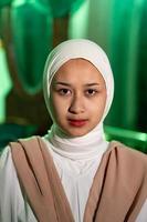 en muslim kvinna med en vit slöja och vit kläder är Sammanträde i de mitten av en grön rum utan smink foto