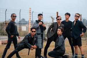 en grupp av Tonårs Pojkar i svart kläder Framställ mycket galant med deras vänner i en fält foto