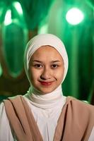 en muslim kvinna med en vit slöja och vit kläder leende mycket Söt utan smink på henne ansikte i en grön rum foto