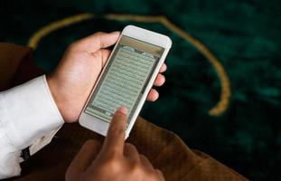 person innehav en quran digital i smartphone foto