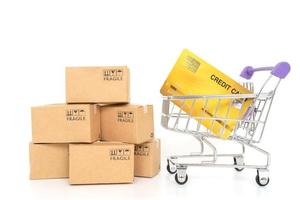papperslådor och ett kreditkort i en vagn på en vit bakgrund. online shopping eller e-handel koncept och leverans servicekoncept foto