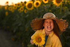 en Lycklig ung flicka med lång hår i en sugrör hatt står i en stor fält av solrosor. sommar dag. en värma solnedgång. foto