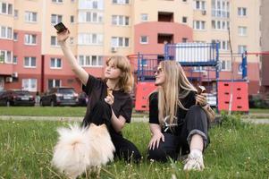 två rolig flickor är äter is grädde och spelar med en pomeranian hund. tar selfies foto