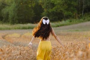en flicka kör genom en fält med spikelets mot de bakgrund av de miljö Sol foto