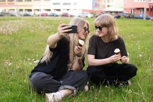 två rolig flickor är äter is grädde och tar selfies på de gata. tonåringar i social nät foto