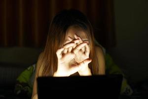 asiatisk kvinnor lida från ansträngda ögon från ser på datorer i låg ljus. Kolla på bio uppkopplad foto