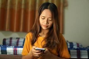 Lycklig asiatisk kvinna ser på de telefon, menande den där vinster är högre, arbete från Hem. foto