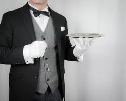 porträtt av butler eller servitör i mörk formell kostym innehav silver- bricka. begrepp av service industri och professionell gästfrihet. foto