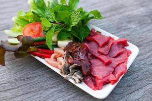 rå nötkött kött nedskärningar skivor på vit tallrik och färsk grönsaker färsk kött topp se - nötkött sashimi , nötkött lever asiatisk thai mat foto