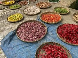 olika grönsaker tomater, chili, röd lök, majs, morot, kalk, vitlök varelse såld på asiatisk traditionell marknadsföra. färgrik grönsaker på runda bambu bricka på traditionell marknadsföra golv foto