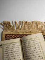 läsning al quran och vändning sida av quran ovan sajadah bön- matta isolerat på vit Plats. vald fokus foto