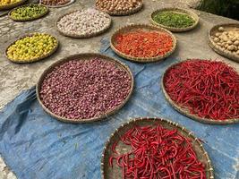 olika grönsaker tomater, chili, röd lök, majs, morot, kalk, vitlök varelse såld på asiatisk traditionell marknadsföra. färgrik grönsaker på runda bambu bricka på traditionell marknadsföra golv foto