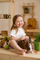 söt liten flicka i de trä- kök av de hus matar de kanin färsk gräs foto
