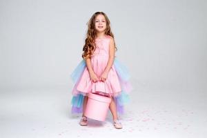 skön liten flicka i en chic rosa klänning poser Sammanträde på en grå bakgrund och kastar konfetti. mode och stil. Plats för text. Foto i de studio. hög kvalitet Foto