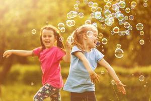 två liten flicka roligt med tvål bubblor i sommar parkera, grön fält, natur bakgrund, vår säsong foto