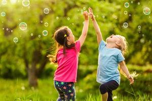 två liten flicka roligt med tvål bubblor i sommar parkera, grön fält, natur bakgrund, vår säsong foto