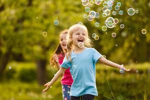 två liten flicka roligt med tvål bubblor i sommar parkera, grön fält, natur bakgrund, vår säsong foto