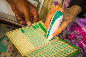 yazd, iran - 22 juni, 2022 - äldre kvinna på Hem använda sig av elektrisk koranen läsa penna till läsa i arabicum foto