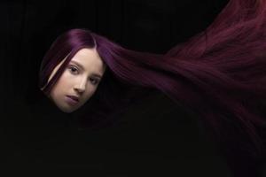 lösa flygande hår. en kvinna med magenta hår utseende på de kamera på en mörk bakgrund. foto