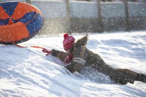 en Lycklig pojke upp i de luft på en rör sledding i de snö.. en pojke diabilder ner en kulle i vinter. foto