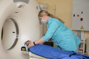 en läkare i en medicinsk klänning förbereder en patient för magnetisk resonans avbildning mri beräknad tomografi i en sjukhus. foto