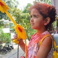 ljuv liten indisk flicka spelar färger på holi festival, innehav pichakaree full av färger, holi festival fester i delhi, Indien foto