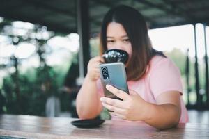asiatisk kvinna innehav och använder sig av mobil telefon i kaffe affär, njuter de smak av kaffe. eller kaffe affär med kopia Plats foto