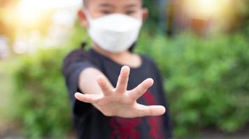 en 5 år gammal asiatisk pojke bär en medicin sjukvård mask och höjer hans hand. do inte närma sig. till upprätthålla social distans till förhindra de spridning av de coronavirus covid-19 foto