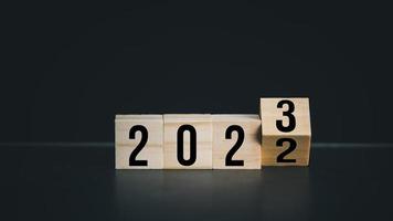 vända av 2022 till 2023 på trä- blockera kub för förberedelse ny år förändra och Start ny företag mål strategi begrepp. på svart bakgrund. foto