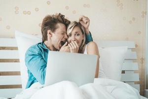 lyckliga par som använder bärbar dator på sängen