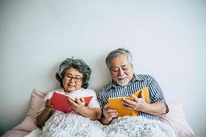 äldre par som ligger på sängen och läser en bok