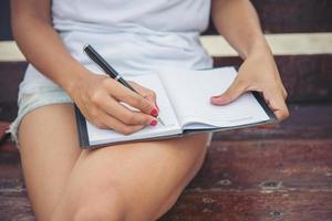ung vacker kvinna som skriver på anteckningsblocket medan du sitter på bänken foto