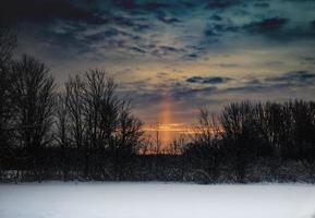 soluppgång med molnig himmel över snöigt fält och träd foto