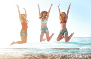 Lycklig leende vänner Hoppar på de strand foto