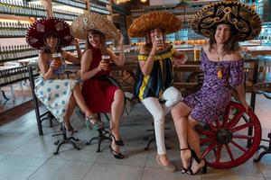 grupp av mogna kvinnor är dricka öl i en pub bär sombreros foto
