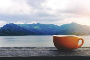 kaffekopp med varm dryck på träbord med utsikt över berget foto