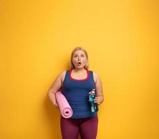 fett flicka gör Gym på Hem. överraskad uttryck. gul bakgrund foto