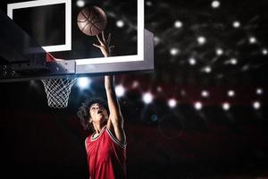 basketboll spelare i röd enhetlig Hoppar hög till göra en slam dunka till de korg foto