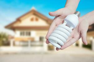 energi sparande begrepp, kvinna hand innehav ljus Glödlampa på hus bakgrund, idéer ljus Glödlampa i de hand foto