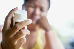 sjuk kvinna innehav piller flaska och läsning recept märka och tittar på medicin sida effekter på Hem hälsa och medicinsk begrepp. foto