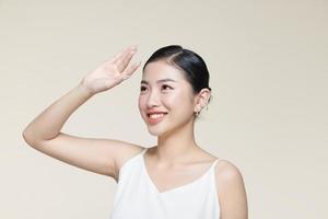 ung asiatisk kvinna höjning hand till beläggning henne ansikte från solljus mot en beige bakgrund foto