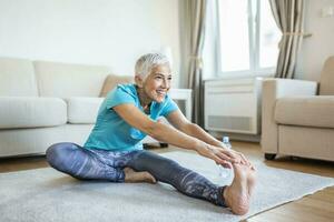 senior kvinna håller på med uppvärmning träna på Hem. kondition kvinna håller på med sträcka övning stretching henne ben, quadriceps .äldre kvinna levande ett aktiva livsstil. foto