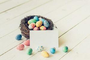 färgrik påsk ägg i de bo och papper kort på trä tabell bakgrund. foto