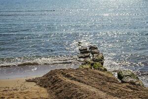 blå vatten bakgrund med stenar på de sandig Strand. hav eller hav landskap foto