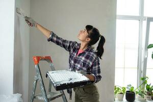 kvinna i måla vält och vit måla målarfärger de vägg av hus på trappstege. konstruktion arbete och kosmetisk reparationer i hus, vägg målning, toning, efterbehandling arbete med din egen händer foto