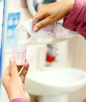 de sjuksköterska händer är häller mors färsk mjölk från de plast väska för mjölk lagring till medicin mätning glas kopp för sjuk nyfödd bebis i de sjukhus. foto