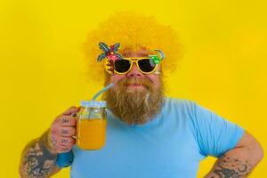 fett Lycklig man med peruk i huvud och solglasögon drycker en frukt juice foto