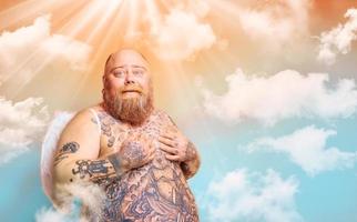 fett förvånad man med skägg , tatueringar och vingar handlingar tycka om ett ängel foto