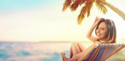 skön flicka Sammanträde på en däck stol på de strand på solnedgång foto